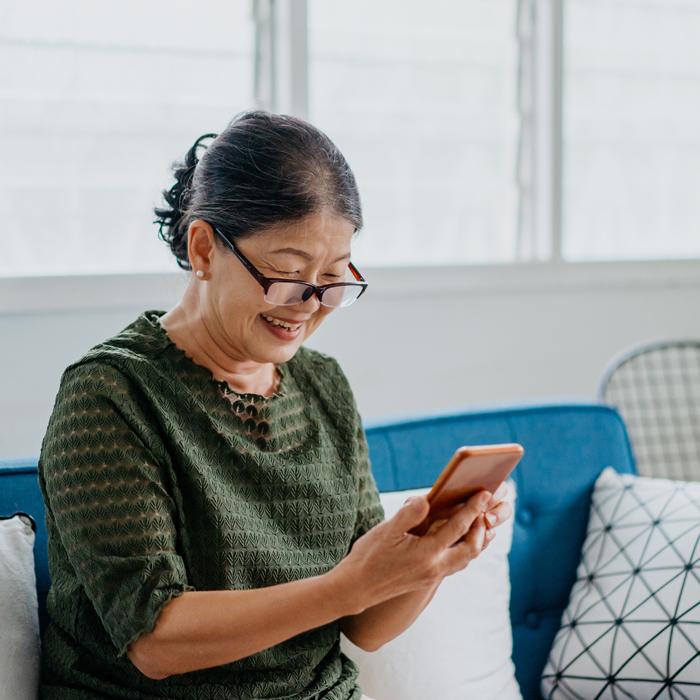 A smiling Patelco member on their couch using the easy-to-use Patelco Mobile App